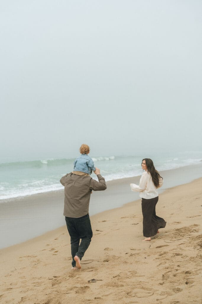 Calafia Beach family photos with toddler and expecting parents walking along shoreline