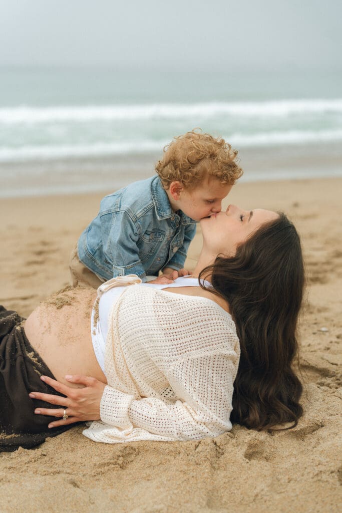 Beach maternity photos with kids – toddler kisses mom’s belly at Calafia Beach in San Clemente