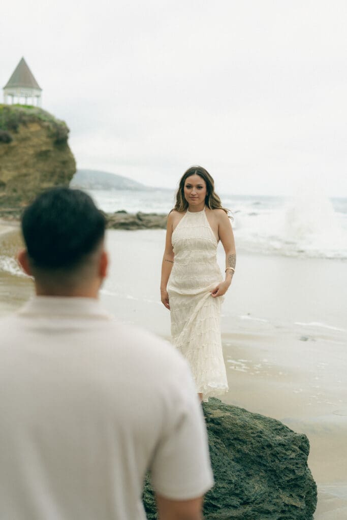 Beach engagement outfits in Laguna Beach: white sundress and tan trousers on rocky shoreline at Shaw’s Cove