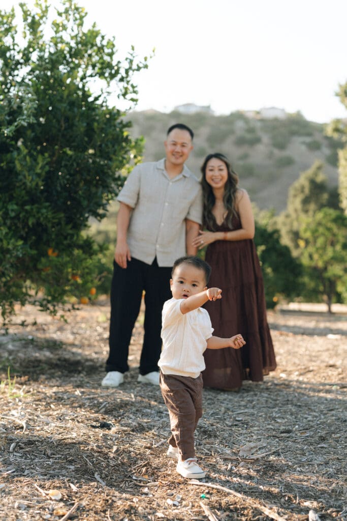 toddler walking in front of parents at family photoshoot in a park