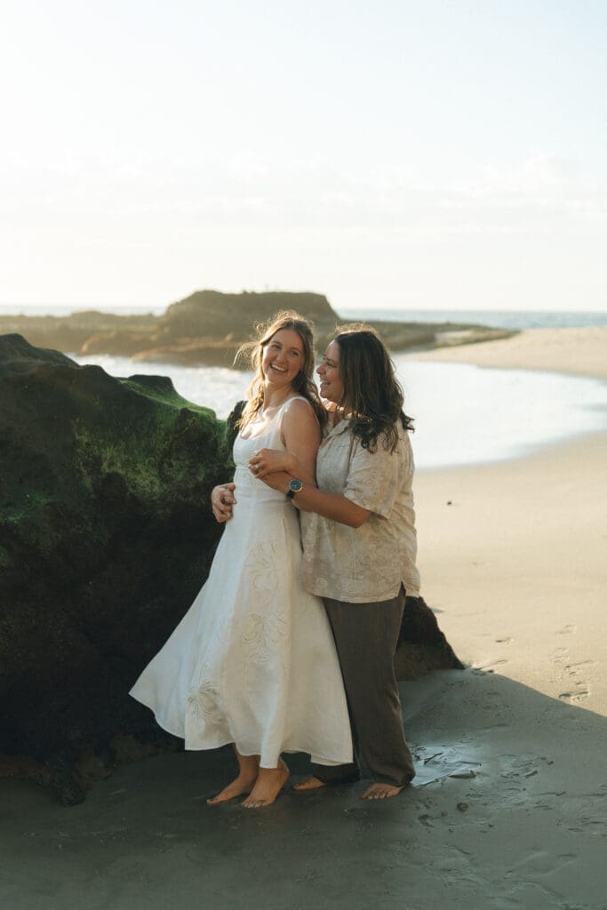 Couple embracing with ocean waves behind them at golden hour