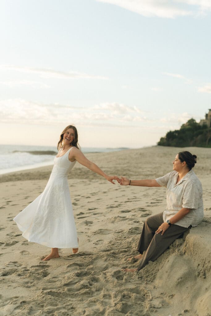 LGBTQ couple holding hands and laughing during beach proposal session